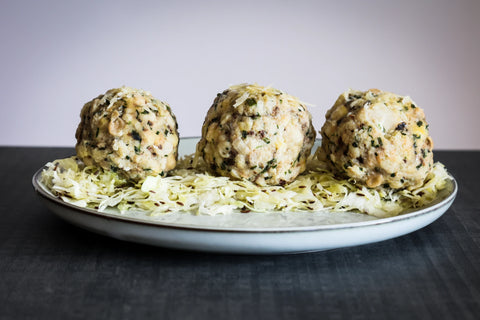 Drei angerichtete Steinpilzknödel auf hellem Teller über fein gehobeltem Weißkraut