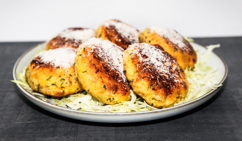 Goldbraun gebratene Käsepressknödel auf Krautsalat, mit geriebenem Käse bestreut, angerichtet auf hellem Teller